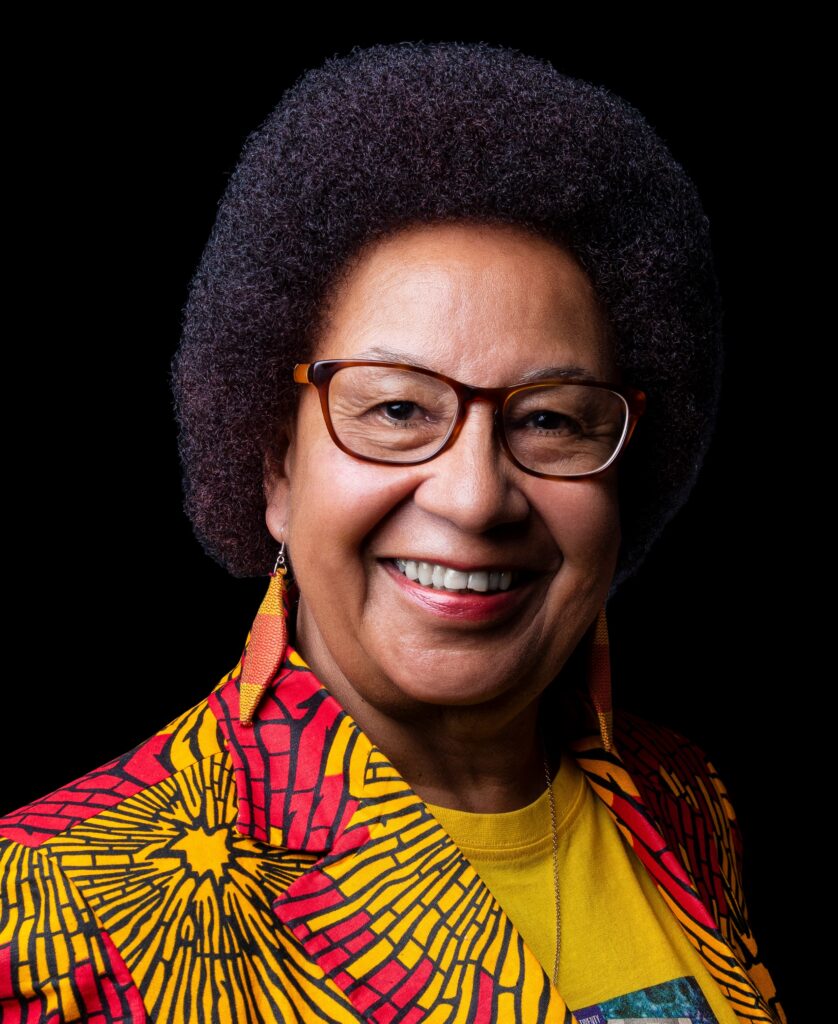 A headshot of a mixed race woman wearing colourful red and yellow shirt.